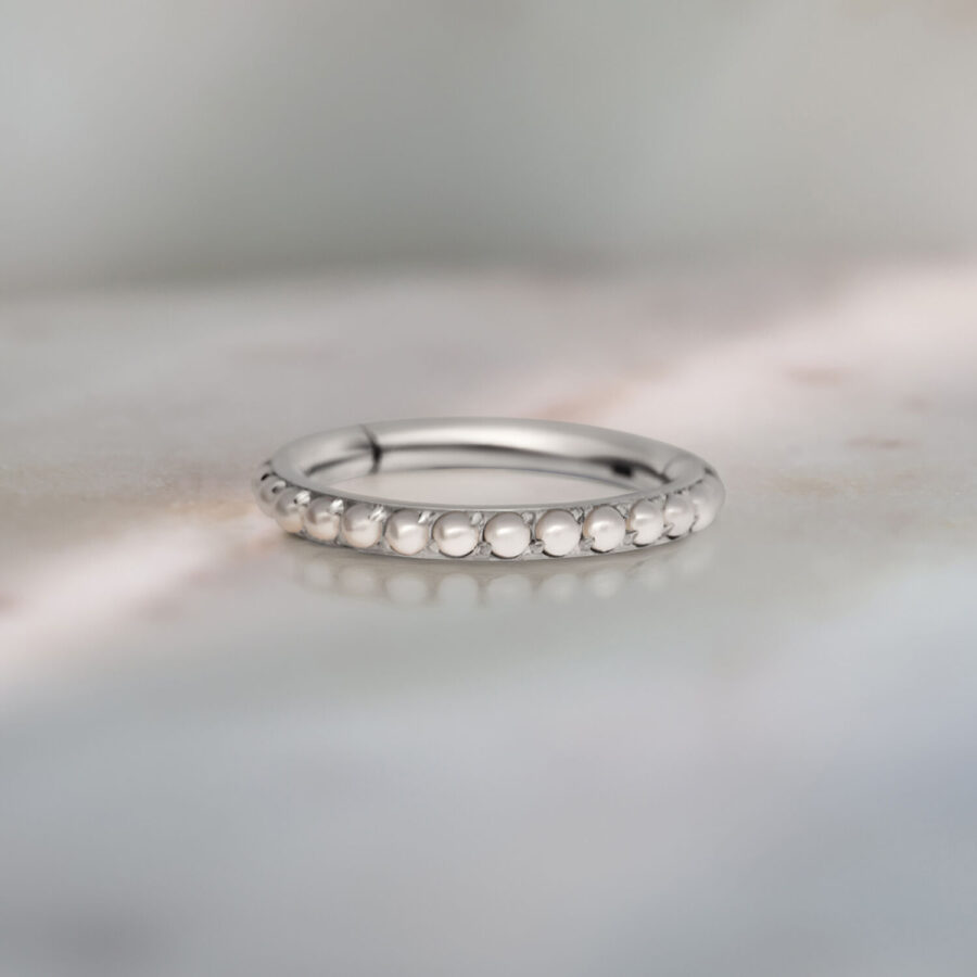 Silberner Piercing-Ring mit Perlenverzierung auf grauem Hintergrund