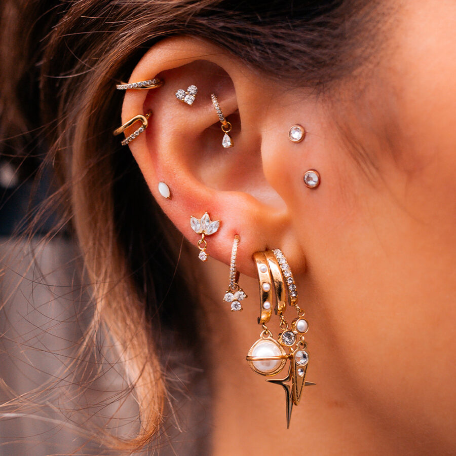 Ohr mit mehreren goldenen Ohrringen und Piercings, helle Haut, brauner Hintergrund