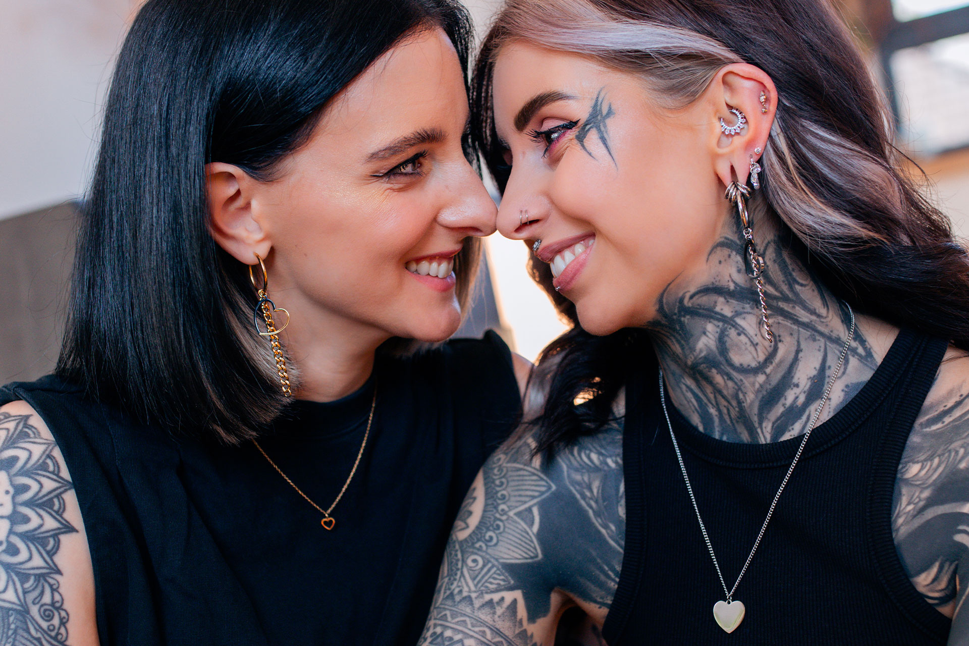 Zwei lächelnde Frauen mit auffälligen Piercings und Tattoos, schwarze Kleidung
