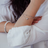 Zweireihiges Herzarmband in Silber Silbernes zweireihiges Armband mit Herzanhänger am Arm einer Person in weißer Kleidung