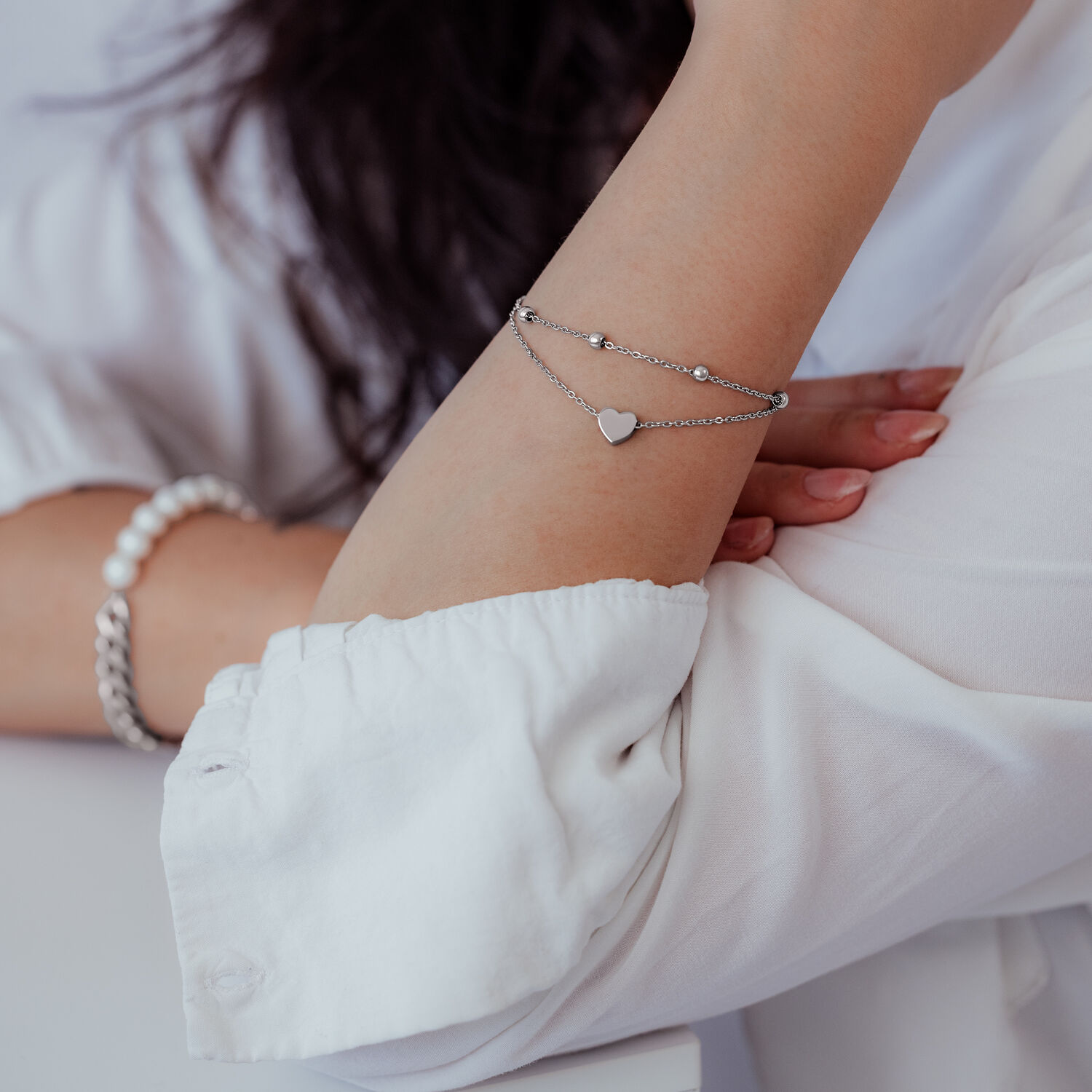 Zweireihiges Herzarmband in Silber Silbernes zweireihiges Armband mit Herzanhänger am Arm einer Person in weißer Kleidung