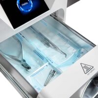 Enbio Autoklav S mit Zubehör im Sterilisationsfach Enbio Autoklav S mit geöffnetem Fach, gefüllt mit Sterilisationswerkzeug auf weißem Hintergrund