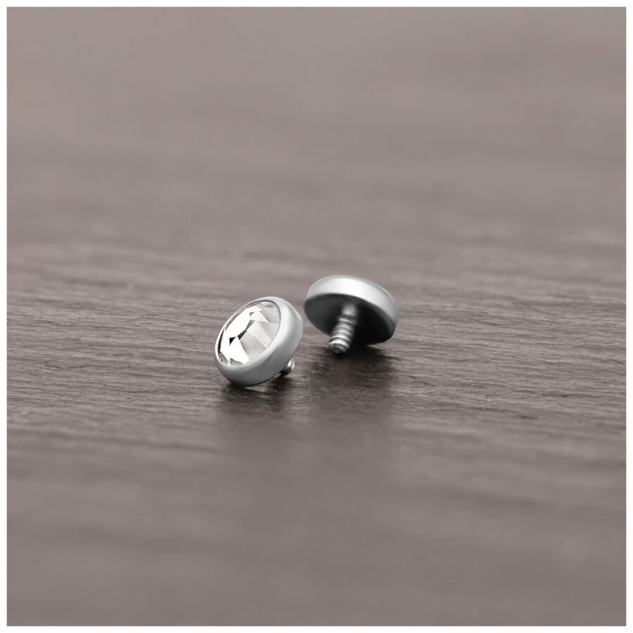 Silberner Piercing-Aufsatz aus Titan mit klarem Kristall auf Holzoberfläche liegend