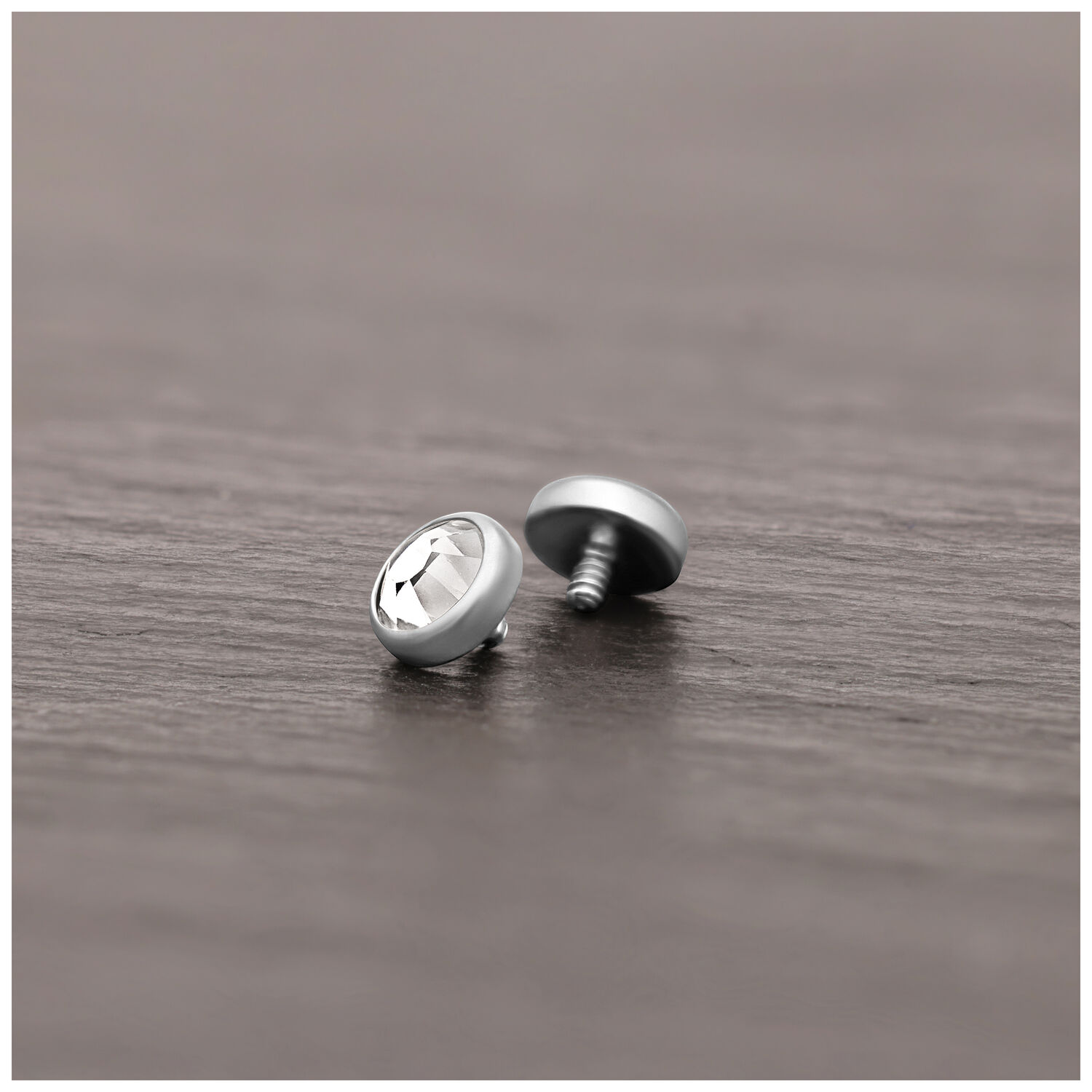 Silberner Piercing-Aufsatz aus Titan mit klarem Kristall auf Holzoberfläche liegend