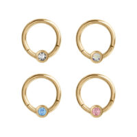 Vier goldene Piercing-Ringe mit klaren, blauen, rosa und schimmernden Kristallen auf weißem Hintergrund