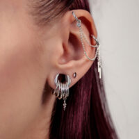 Silberne Piercingkette am Ohr mit Ketten Nahaufnahme eines Ohres mit silberner Piercingkette und mehreren silbernen Ringen