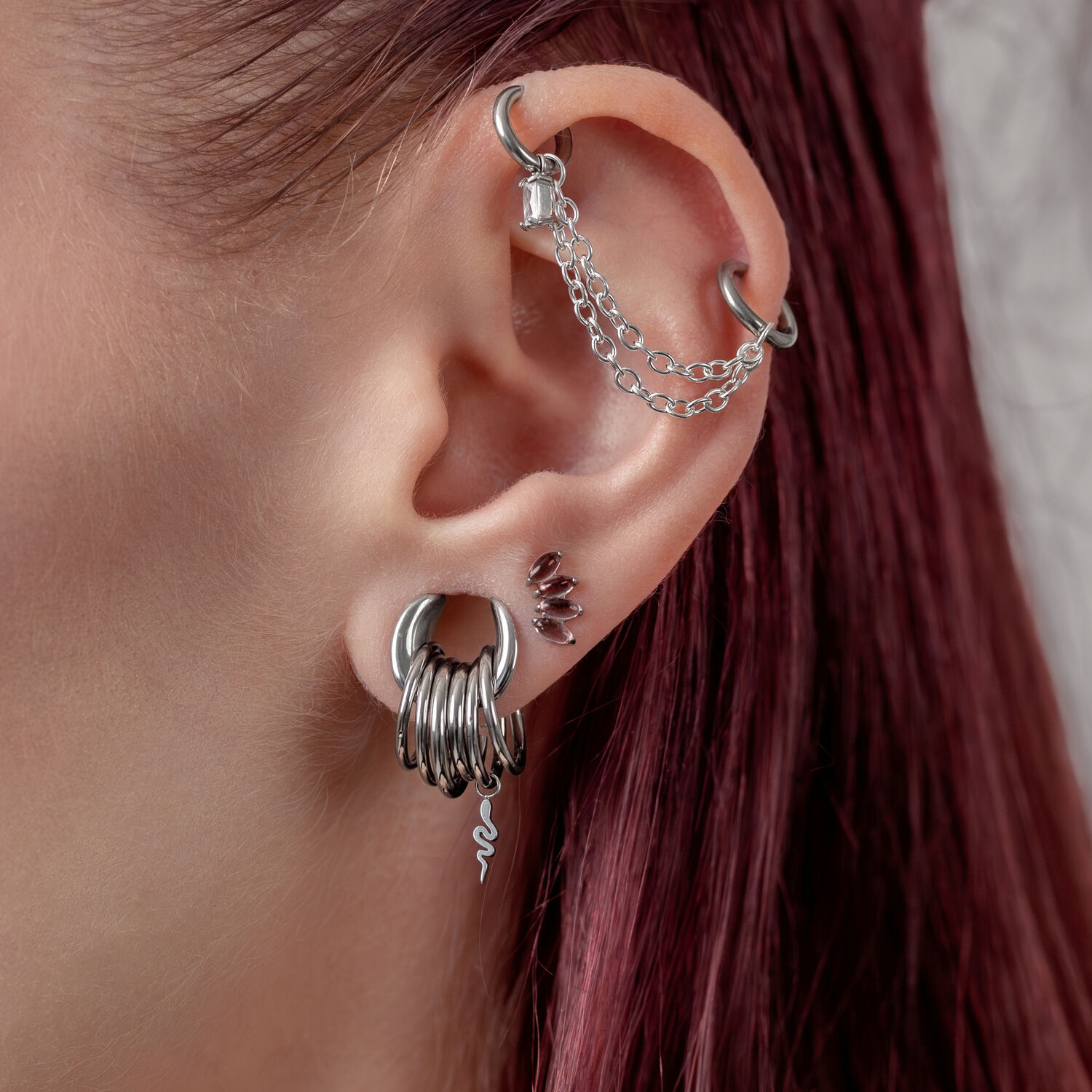 Doppelte Piercingkette aus Silber Ohr mit mehreren silbernen Piercings und einer Kette auf weißem Hintergrund