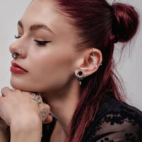 Eleganter Kristall-Piercing-Anhänger in Silber und Gold Frau mit eleganten Ohrpiercings und Kristall-Anhängern, rotes Haar