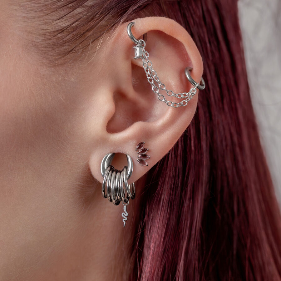 Ohr mit mehreren silbernen Piercings, darunter ein Schlangenanhänger, auf rotem Haar