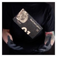 Piranha Latex-Handschuhe Schwarz 100 Stück Person in schwarzem Shirt hält schwarze Piranha Latex-Handschuhe Schachtel vor dunklem Hintergrund