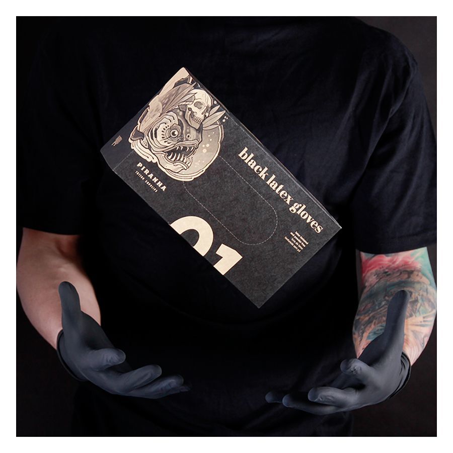 Piranha Latex-Handschuhe Schwarz 100 Stück Person in schwarzem Shirt hält schwarze Piranha Latex-Handschuhe Schachtel vor dunklem Hintergrund