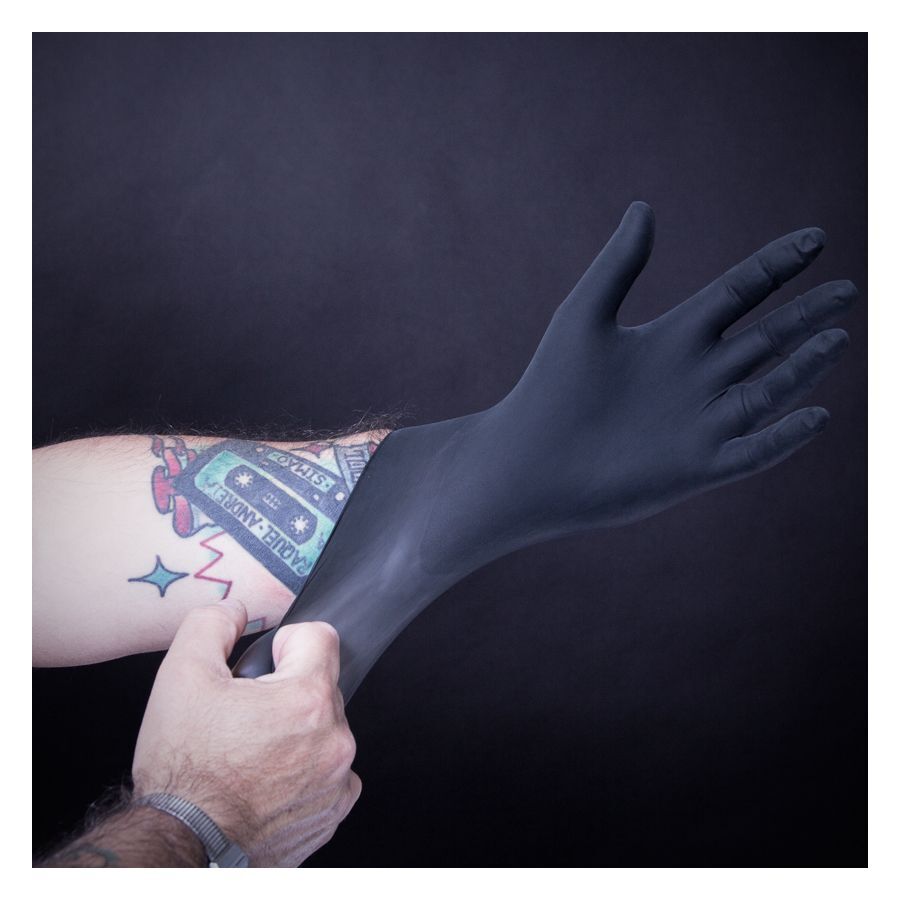 Schwarze Latexhandschuhe Wildcat Piranha Schwarzer Latexhandschuh wird über tätowierten Arm gezogen