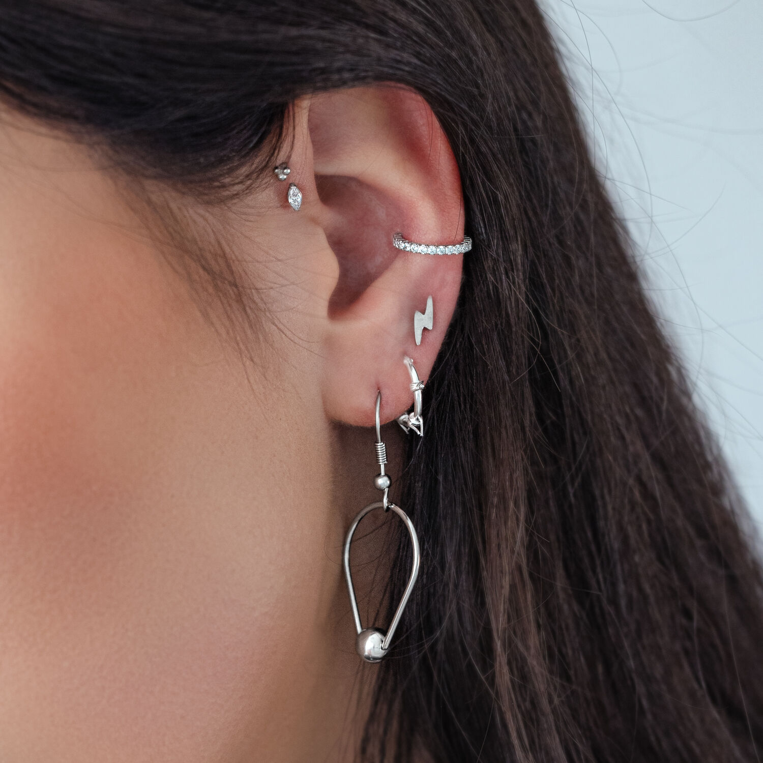 Silberne Ohrpiercings mit Kristallen Nahaufnahme eines Ohres mit mehreren silbernen Piercings, einschließlich eines Kristallaufsatzes