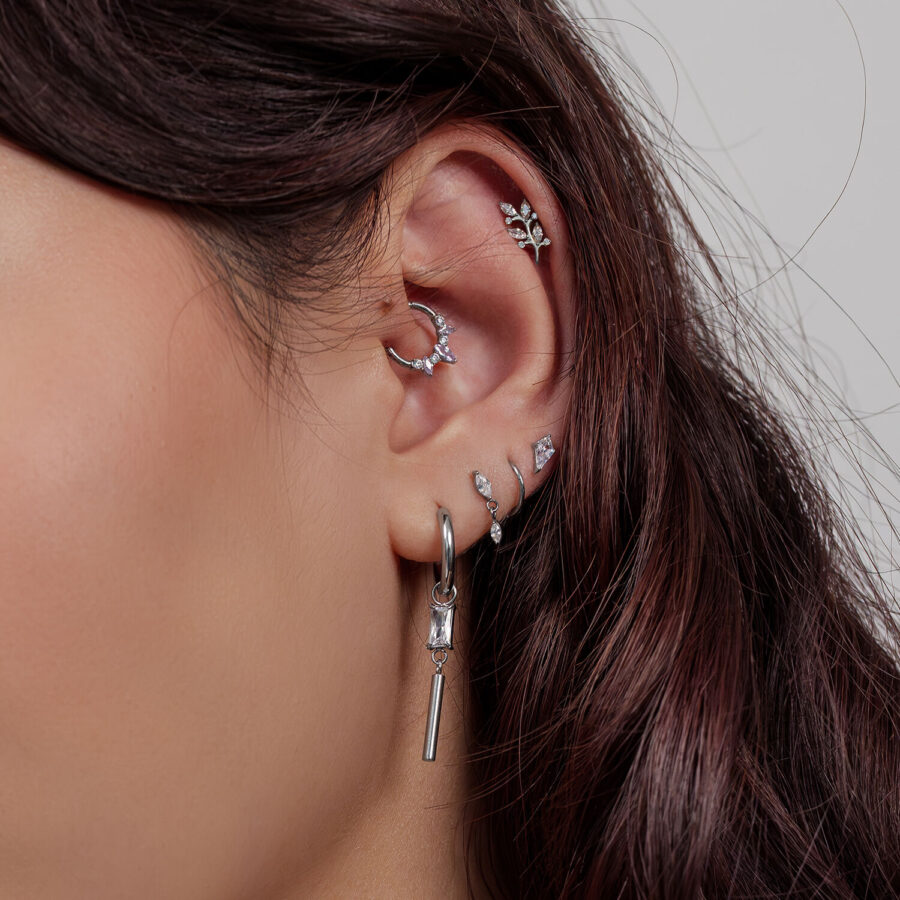 Ohr mit mehreren silbernen Piercings, darunter Kristallblatt-Designs, auf hellem Hintergrund
