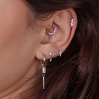Nahaufnahme eines Ohres mit mehreren silbernen Piercings, einige mit Kristallen besetzt