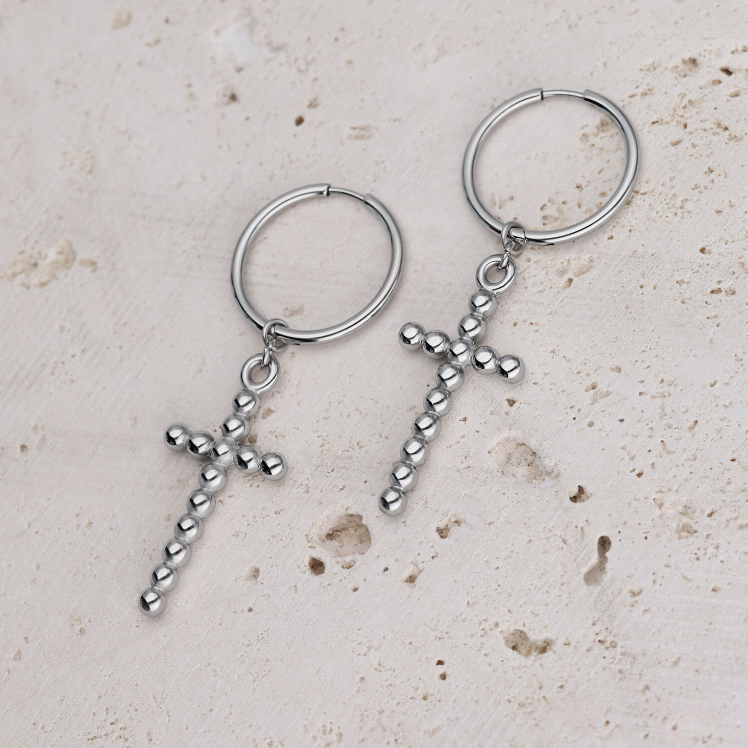 Silberne Bubble Cross Hoops Ohrringe Zwei silberne Creolen mit Kreuzanhängern auf hellem Stein