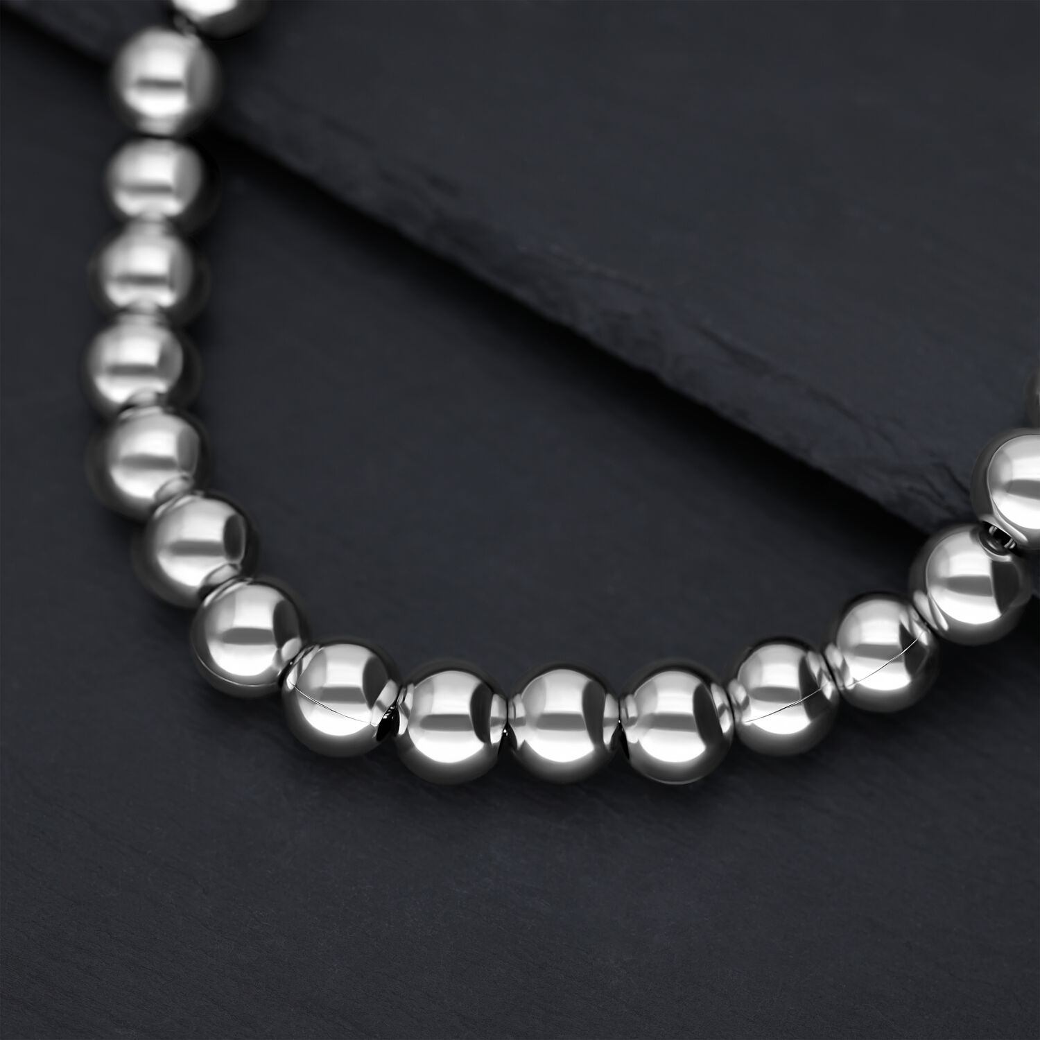 Silberne Bubble Kette aus Chirurgenstahl Nahaufnahme einer silbernen Kette aus glänzenden Metallkugeln auf dunklem Hintergrund