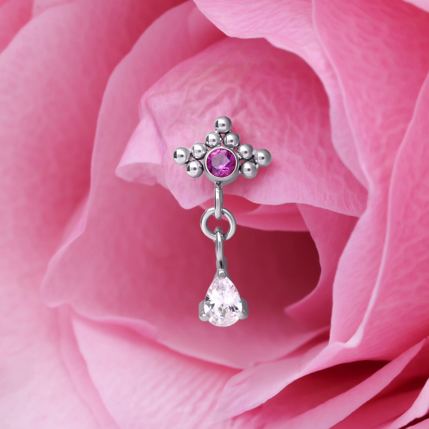 Silberner Piercing Anhänger mit rotem Kristall Silberner Piercing Anhänger mit rotem Kristall und Tropfenform Anhänger vor rosa Blütenblatt