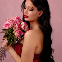 Frau mit Rosenstrauß in rotem Kleid Frau mit langen, dunklen Haaren hält einen Strauß rosa Rosen vor rosa Hintergrund.