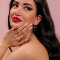 Silberner Push Fit Aufsatz mit rotem Kristall Frau mit langen schwarzen Haaren, roten Lippen und silbernem Ohrring mit rotem Kristall vor rosa Hintergrund