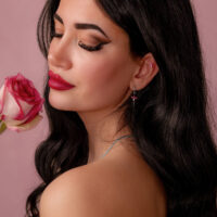 Silberner Push Fit Aufsatz mit rotem Kristall Frau mit langen dunklen Haaren hält eine rosa Rose und trägt einen silbernen Ohrring mit rotem Kristall auf rosa Hintergrund