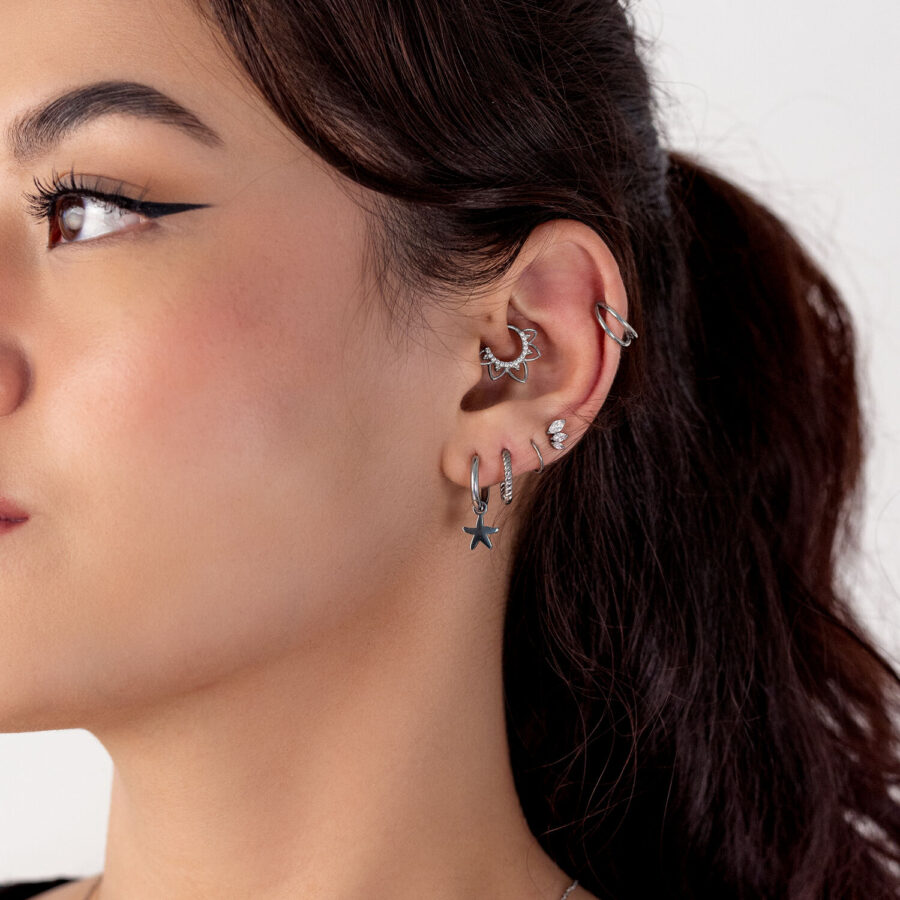 Nahaufnahme eines Ohres mit mehreren silbernen Piercings, darunter ein Sternanhänger, auf weißem Hintergrund