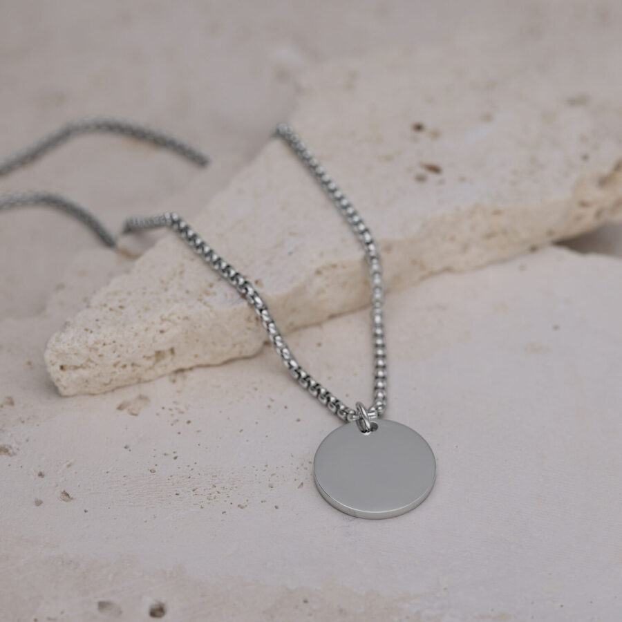 Silberne Kette mit rundem Anhänger auf hellem Steinboden