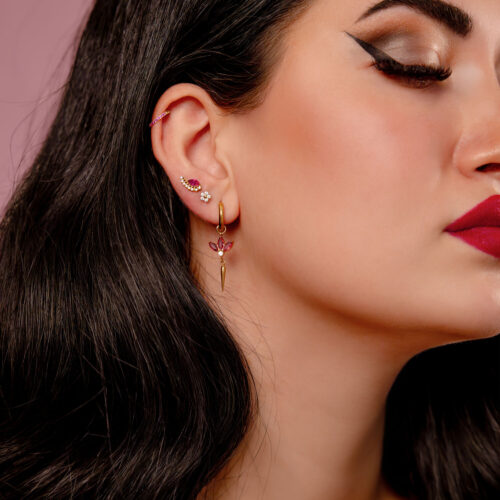 Nahaufnahme von Ohren mit goldenen Piercing-Ohrringen und roten Kristallen, auf rosa Hintergrund
