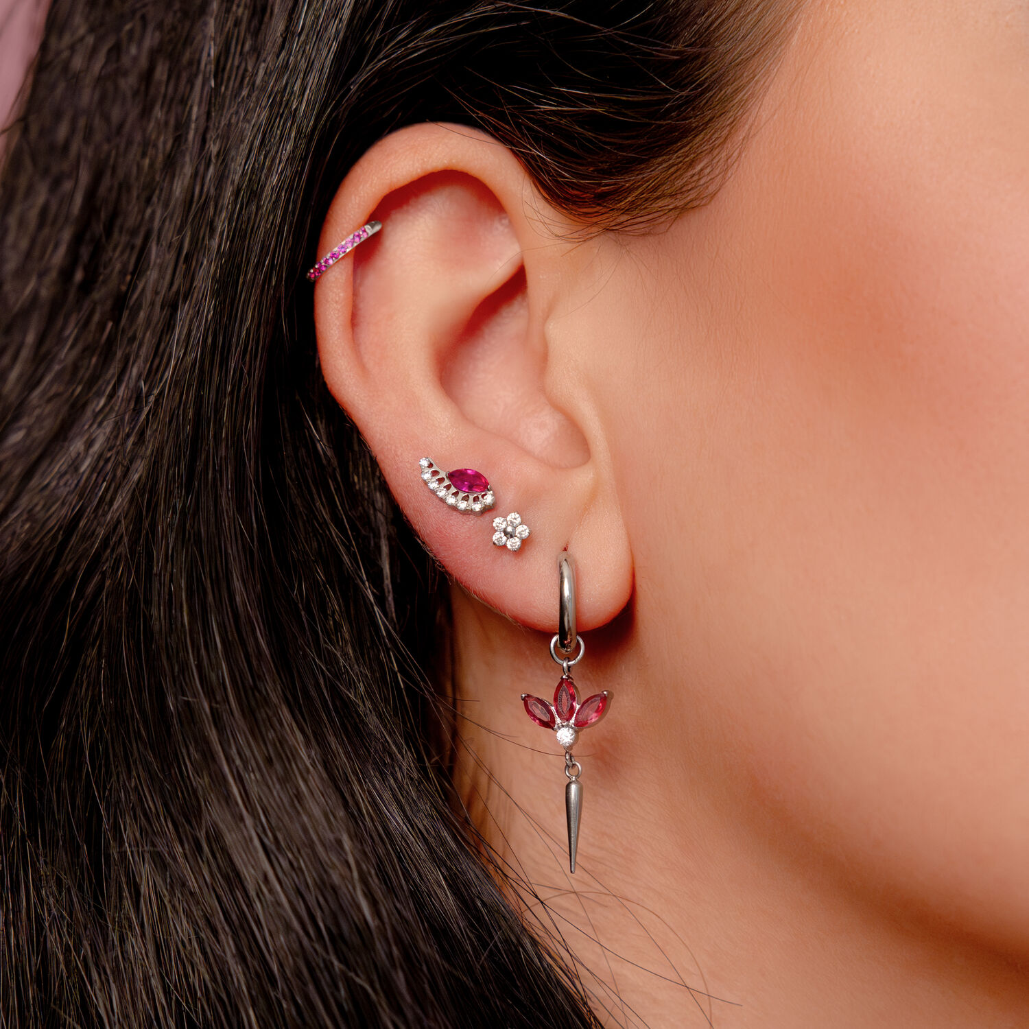 Silberner Ohrring mit roten Kristallen Silberner Ohrring am Ohr mit roten Kristallen und mehreren Piercings in einem Ohr