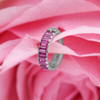 Silberner Piercing-Ring mit roten Baguette-Kristallen auf rosa Blütenhintergrund