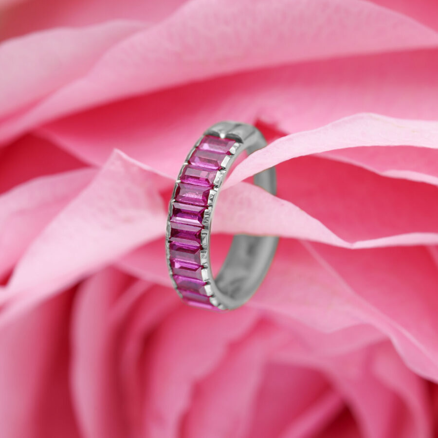 Silberner Piercing-Ring mit roten Baguette-Kristallen auf rosa Blütenhintergrund
