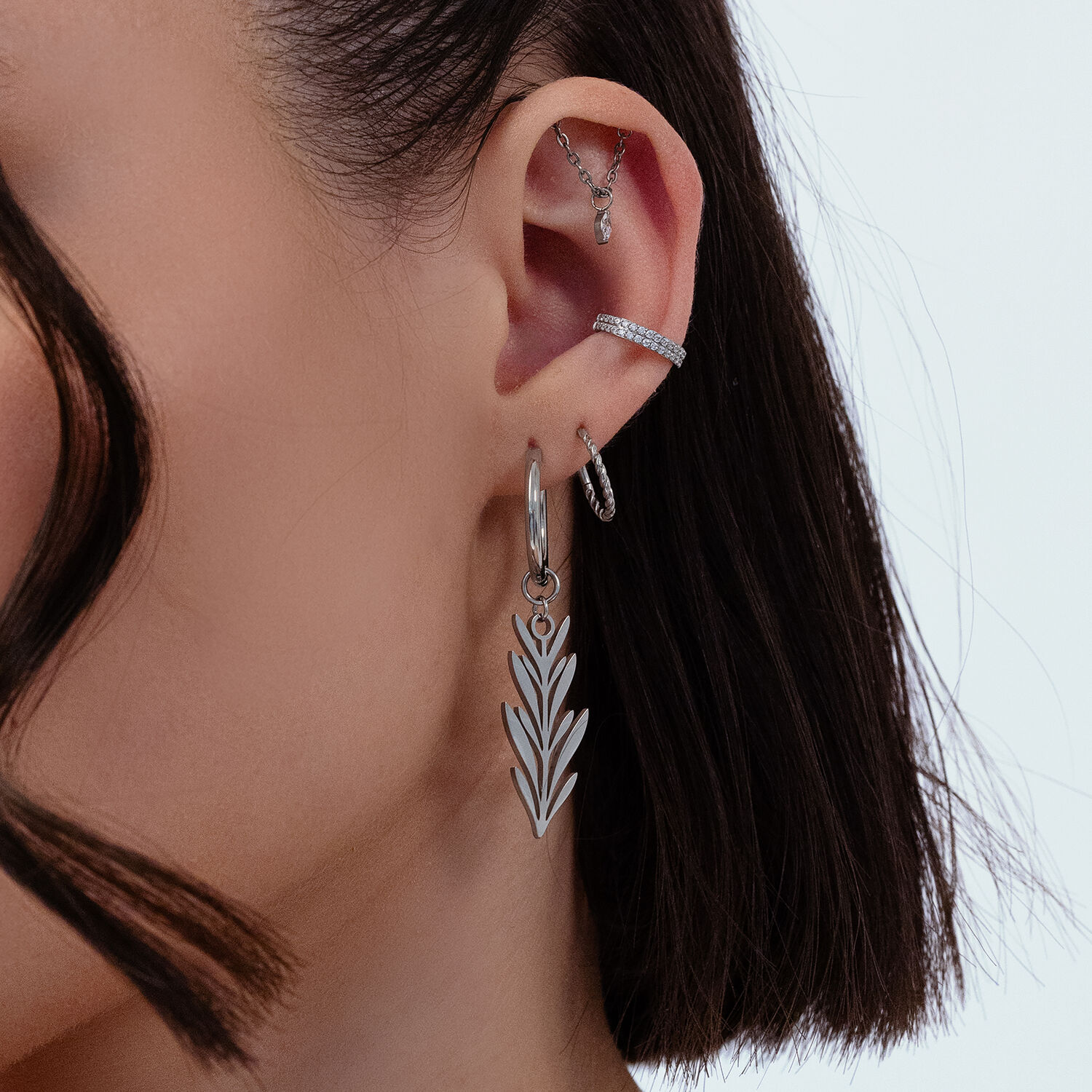 Silberne Ohrhänger mit Blattdesign Nahaufnahme eines Ohrs mit silbernen Ohrringen im Blattdesign, mehrere Piercings