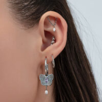 Silberne Schmetterling Creolen am Ohr Nahaufnahme eines Ohres mit silbernen Creolen, Schmetterlingsanhänger und mehreren Piercings vor hellem Hintergrund