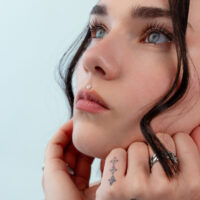 Push Fit Blumenaufsatz in Silber Nahaufnahme eines Gesichts mit silbernem Blumen-Piercing an der Nase, hellblauer Hintergrund