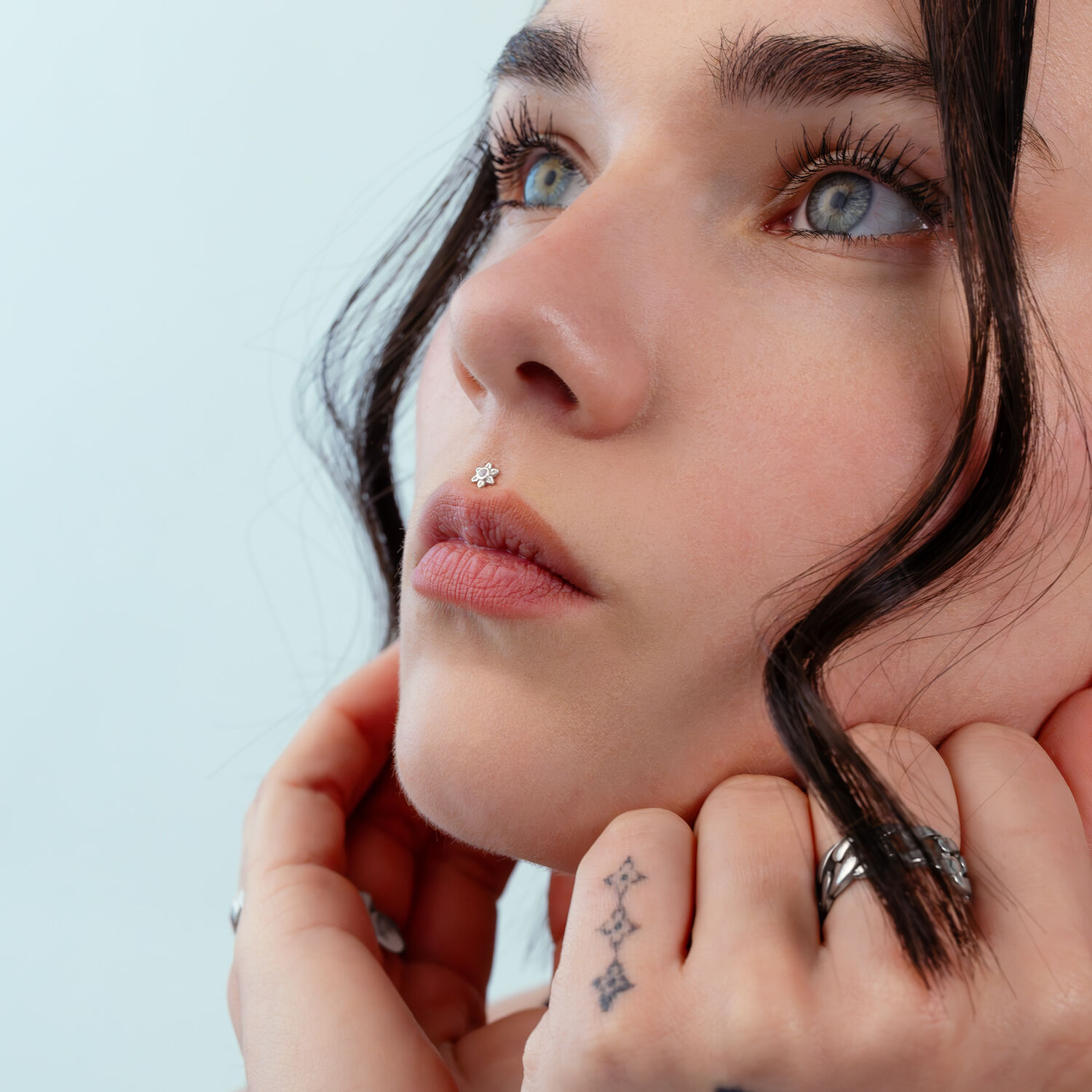 Push Fit Blumenaufsatz in Silber Nahaufnahme eines Gesichts mit silbernem Blumen-Piercing an der Nase, hellblauer Hintergrund