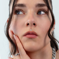 Silbernes Blatt-Piercing Aufsatz Nahaufnahme eines Gesichts mit silbernem Blatt-Piercing an der Nase, Haare im Hintergrund