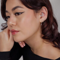 Silberner Ohr-Piercing mit Mond-Design Frau mit mehreren silbernen Piercings, darunter ein mondförmiges Design am Ohr auf hellem Hintergrund