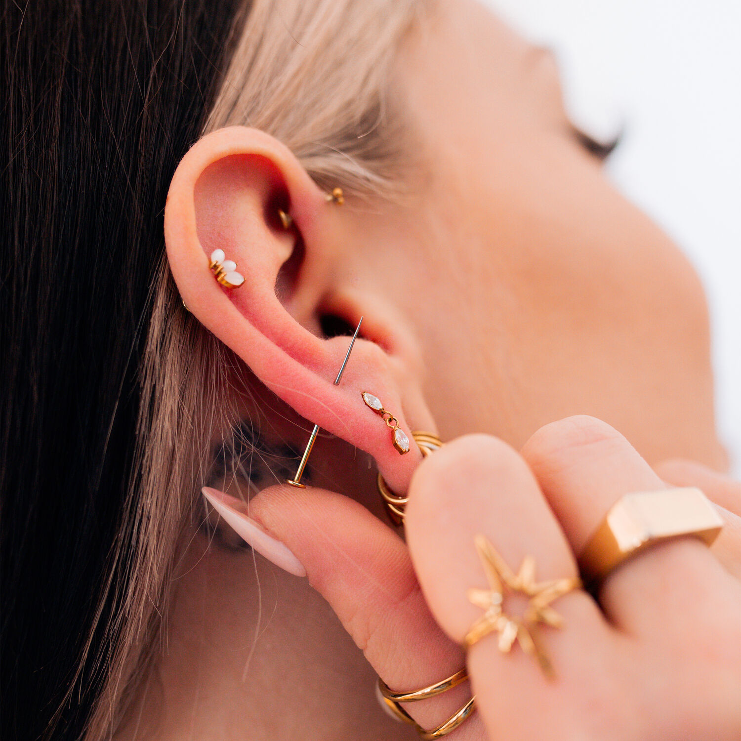 Goldene Piercings am Ohr mit Schmuck Nahaufnahme eines Ohrs mit mehreren goldenen Piercings und Schmuckstücken, Hand hält das Ohr