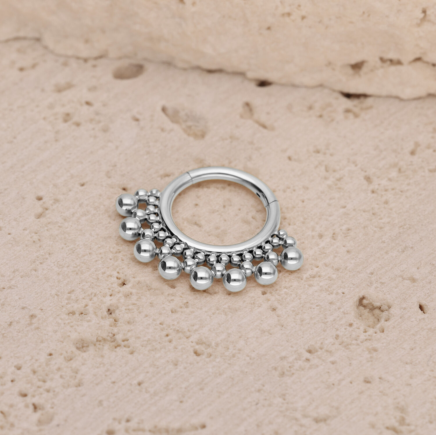 Silberner Titan Septum Clicker mit Kugeln Silberner Septum Clicker mit kleinen Kugeln auf einem strukturierten Steinuntergrund