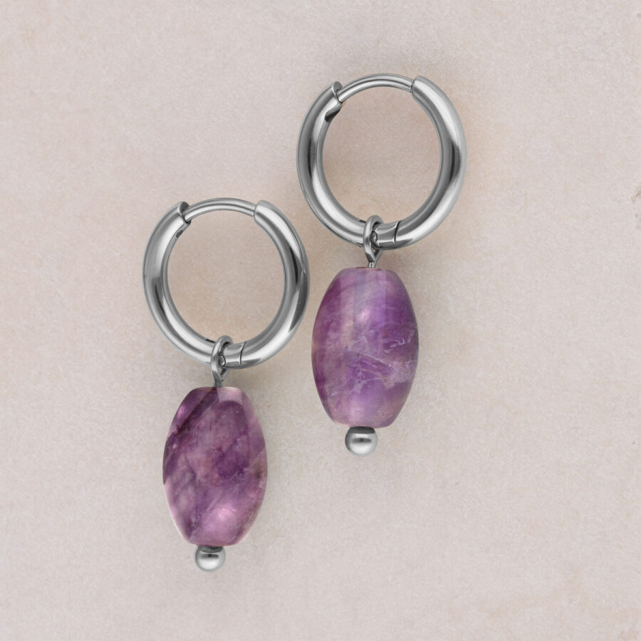 Zwei silberne Creolen mit violettem Amethystanhänger auf beigem Hintergrund