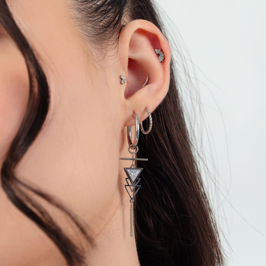 Frau mit silbernen Artdeco Ohrringen und mehreren Ohrpiercings vor weißem Hintergrund
