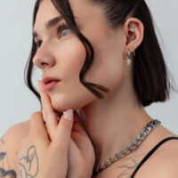 Frau mit silbernen Ohrringen mit Symbolen und Kettenhalskette, Tattoos auf der Hand