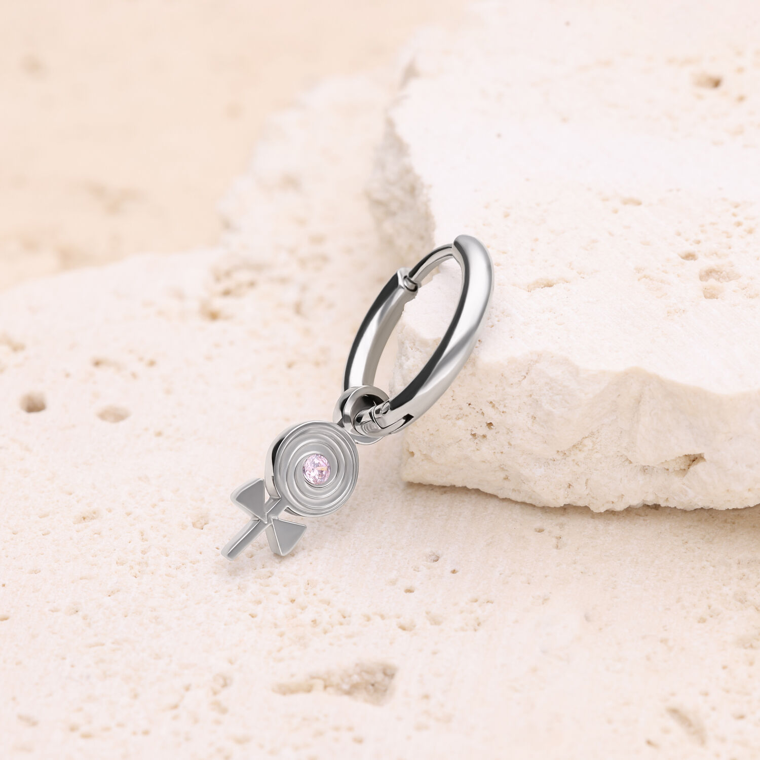 Silberner Ring mit Venus-Symbol-Anhänger und kleinem Kristall, auf hellem Stein