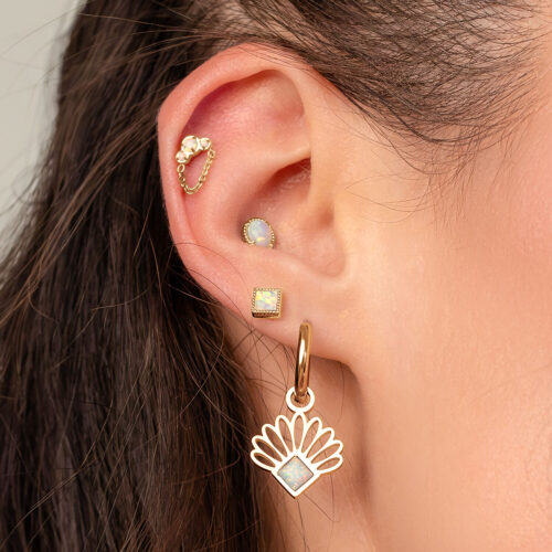 Ohr mit goldenen Opal-Piercings, darunter ein Kettenaufsatz und ein großer hängender Ohrring.
