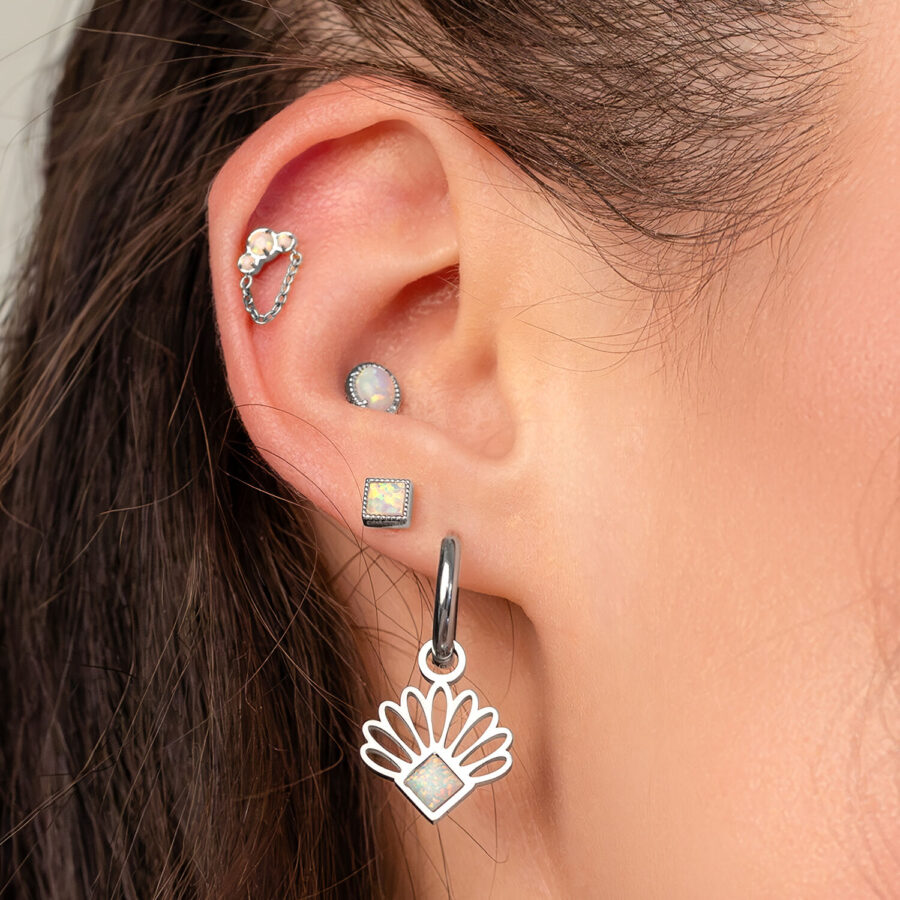 Nahaufnahme eines Ohrs mit mehreren Piercings, darunter ein Opal-Piercing mit Kettenaufsatz