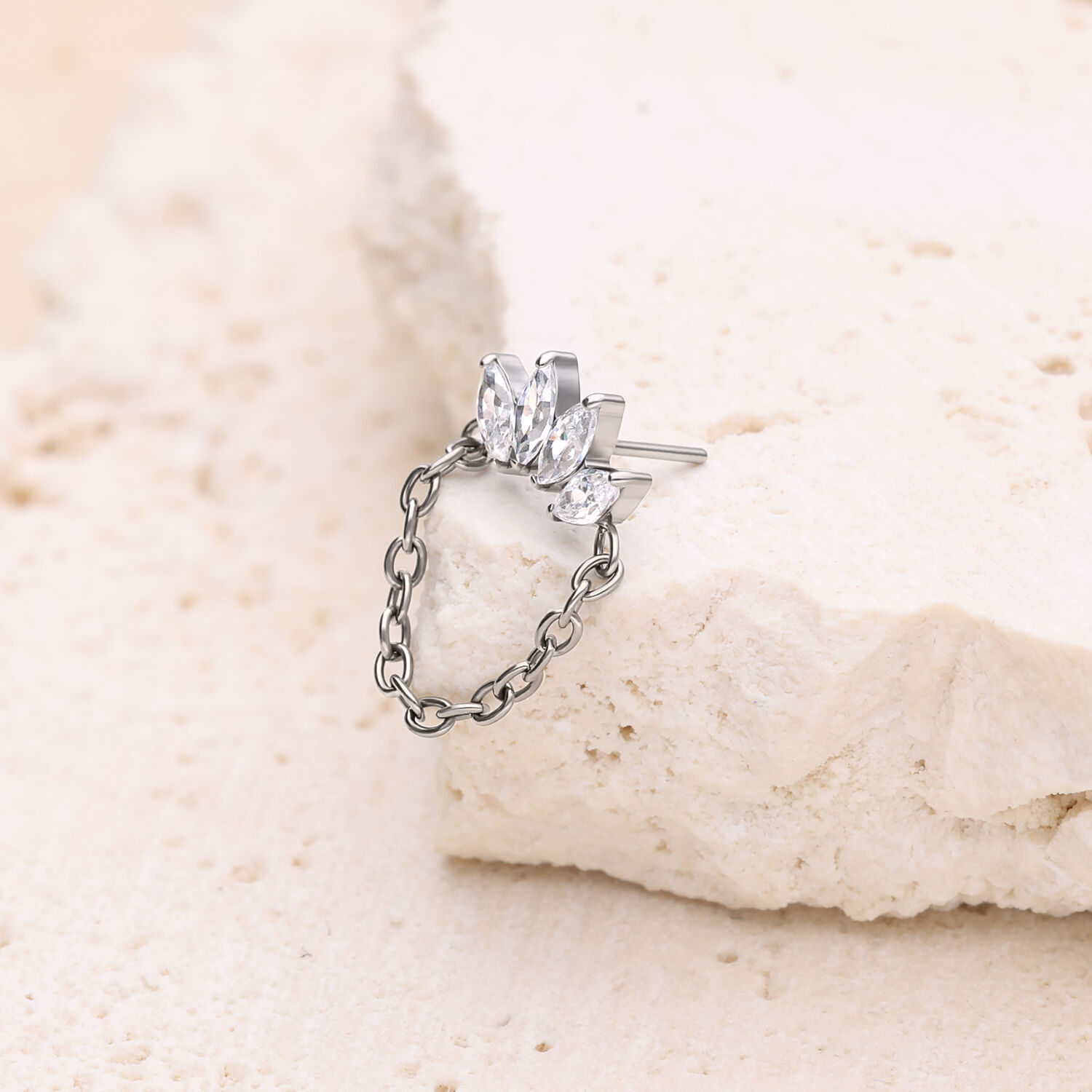 Silberner Ohrstecker mit funkelnden Kristallen und Kette auf hellem Stein