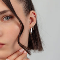 Silberne Creolen und Ohrpiercing Nahaufnahme eines Ohres mit silbernen Creolen und mehreren Ohrpiercings vor grauem Hintergrund.