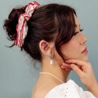 Haaraccessoire mit rotem Band Frau mit hochgestecktem Haar, rotem Haarband und Perlenohrring vor grauem Hintergrund