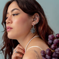 Silberner Push Fit Grape Aufsatz Frau mit mehreren silbernen Piercings im Ohr, trägt eine Perlenkette und hält Trauben.