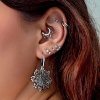 Silberne Ohrpiercings mit Blumenanhänger Nahaufnahme eines Ohrs mit mehreren silbernen Piercings, darunter ein großer Blumenanhänger, auf hellem Hintergrund
